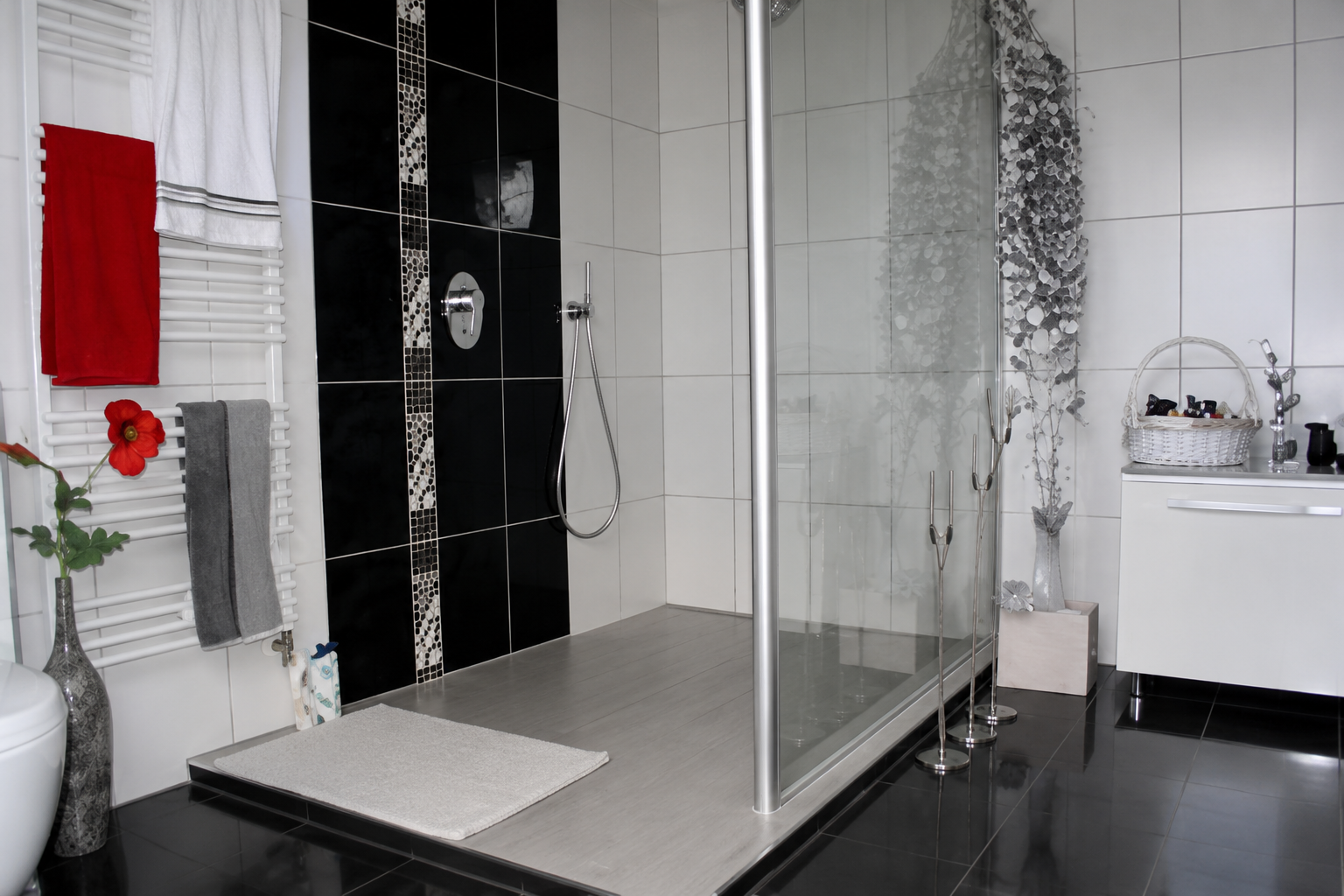Modernes Bad mit schwarzen und weißen Fliesen sowie dekorativen Mosaikstreifen in der Dusche.