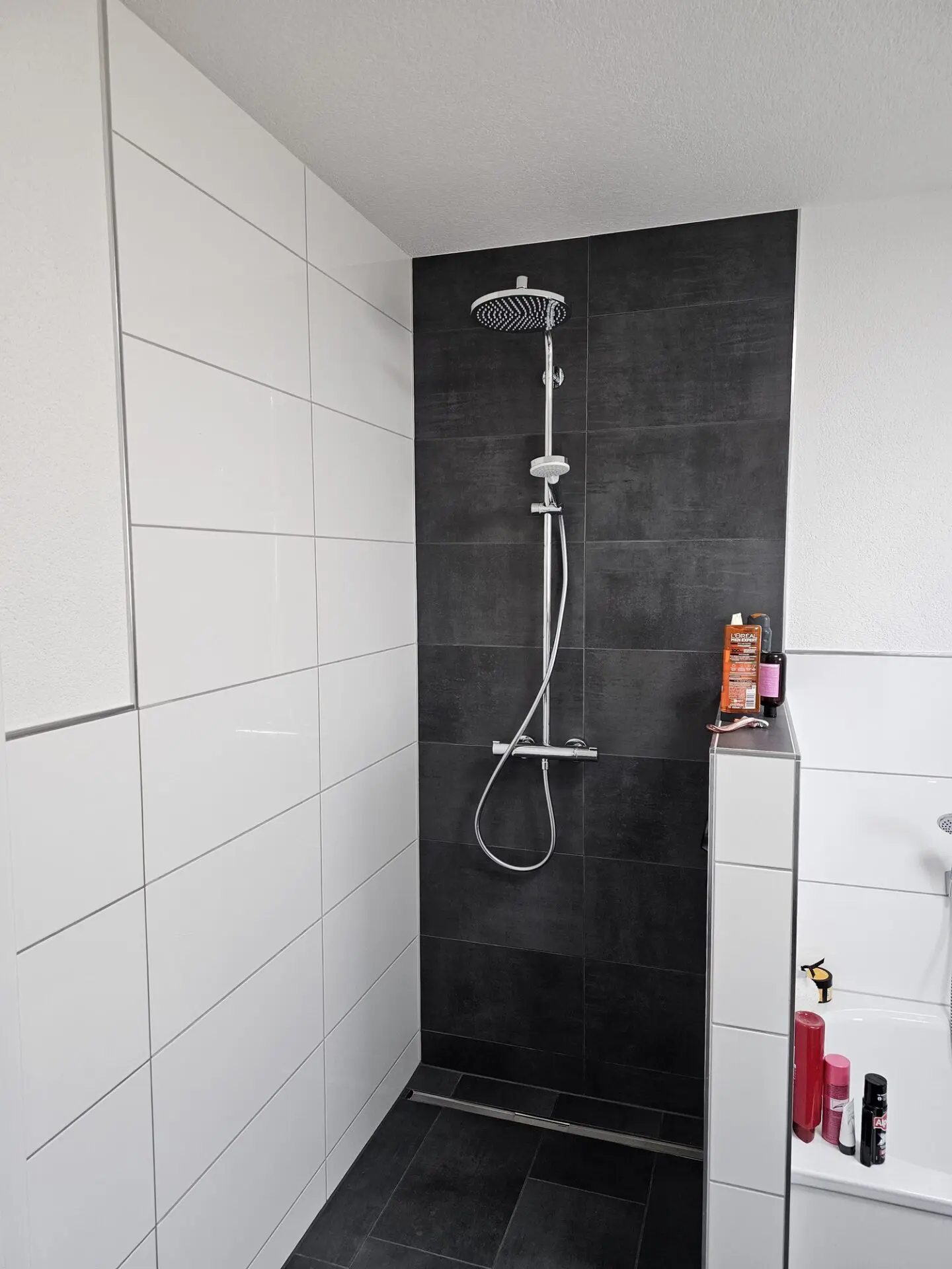 Moderne bodengleiche Dusche mit weißen Wandfliesen, dunkler Fliesenwand und Regendusche.
