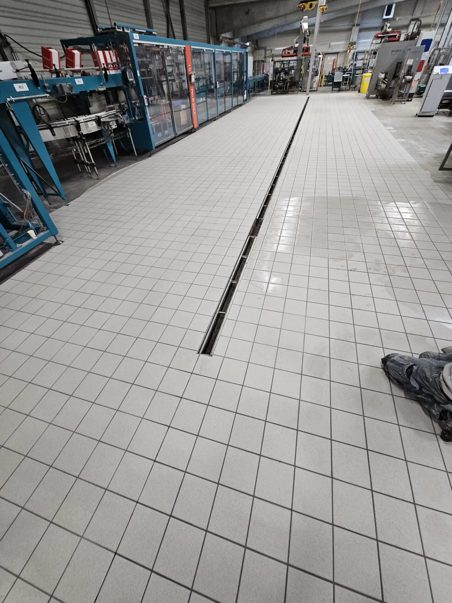 Gefliester Boden einer Industriehalle mit zentraler Entwässerungsrinne zwischen Produktionsanlagen.