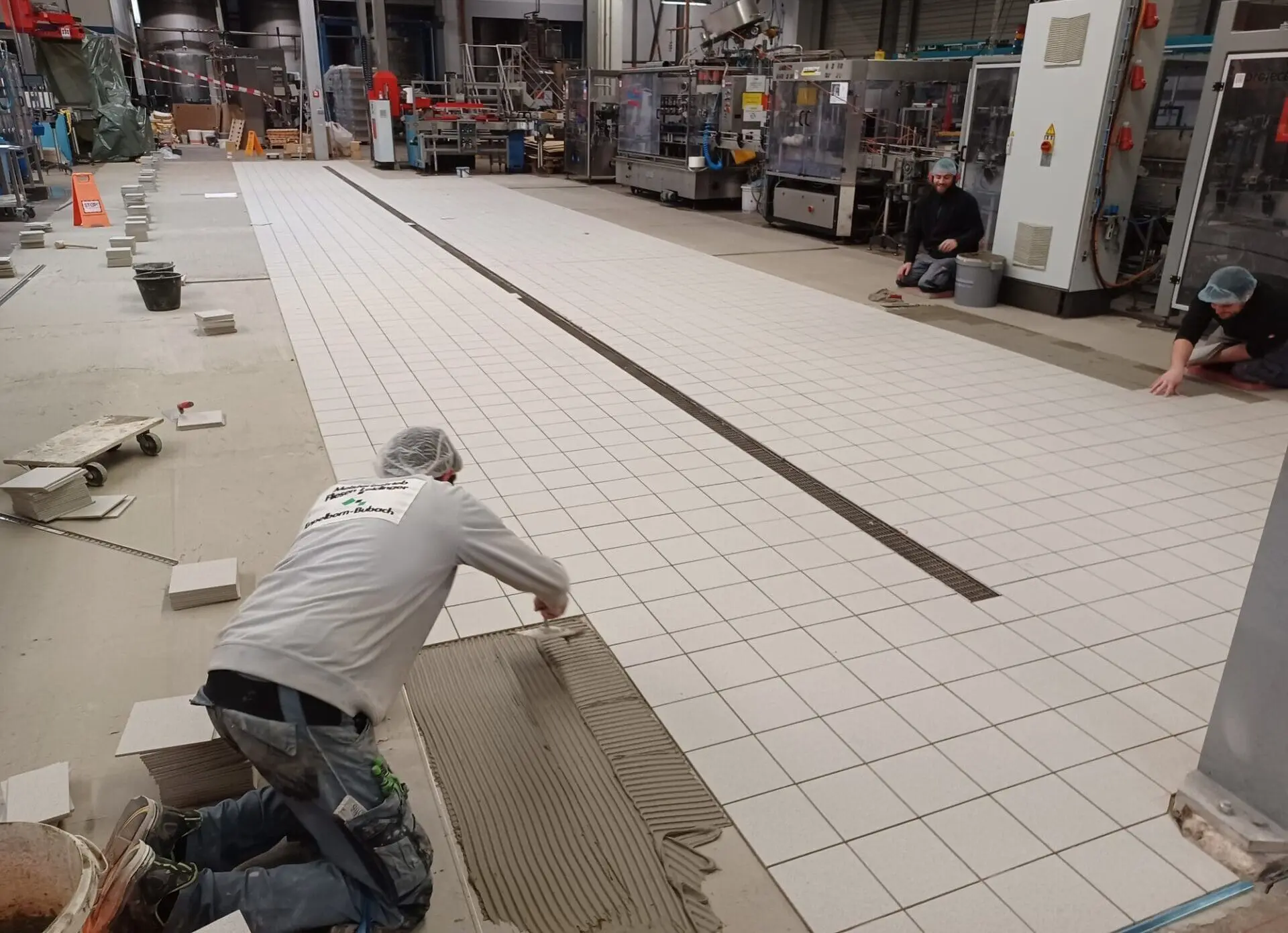 Fliesenleger bei der Verlegung eines großflächigen Industriebodens mit Entwässerungsrinne.