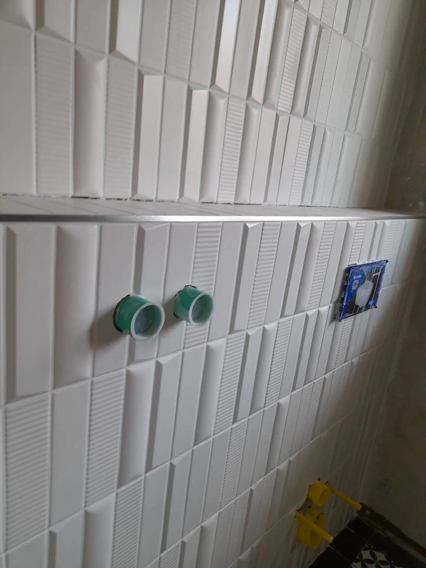 Weiße dreidimensionale Strukturfliesen mit geometrischem Muster an einer Badezimmerwand.