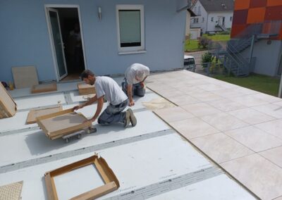 Zwei Fliesenleger bei der Verlegung heller, großformatiger Terrassenfliesen.